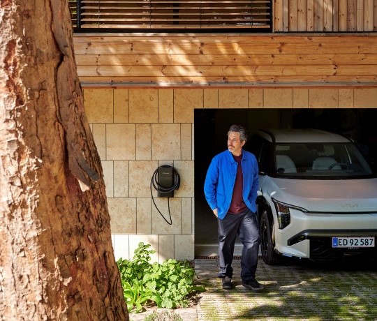 Man i blå jakke kommer ud fra garage med hvid elbil og clever boks