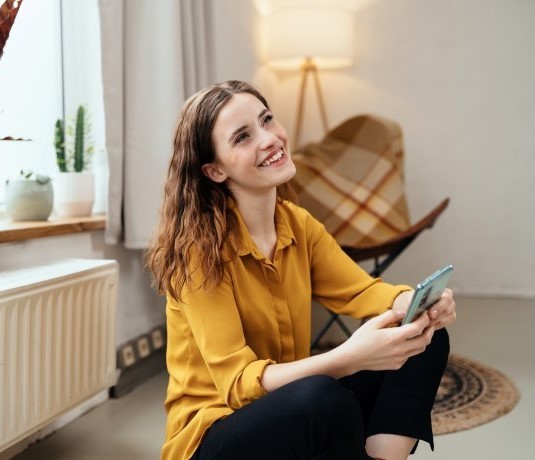 Kvinde sidder på gulvet og nyder varmen fra sin radiator