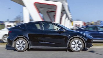 Sort Tesla Model Y kører forbi en lynladestation