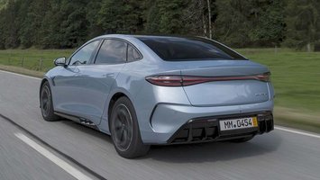 BYD Seal set bagfra, mens  den kører på en landevej med træer i baggrunden