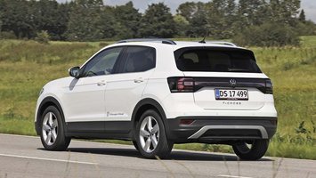 En hvid VW T-Cross set bagfra, mens den kører på en landevej med græs i baggrunden.