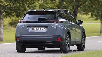 Elbilen Peugeot E-2008 set bagfra, mens den kører ned ad en landevej med træer i baggrunden.