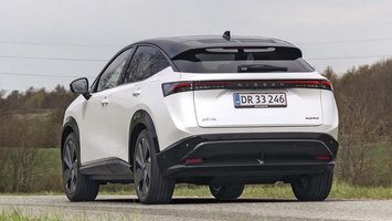 En hvid Nissan Ariya elbil set bagfra, mens den kører på en landevej.