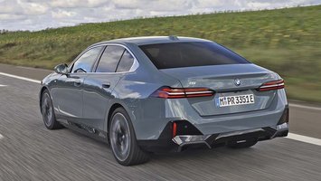 Elbilen BMW i5 set bagfra, mens den kører på en landevej med græs i baggrunden.