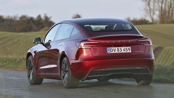 En rød Tesla Model 3 set bagfra, mens den kører på en vej