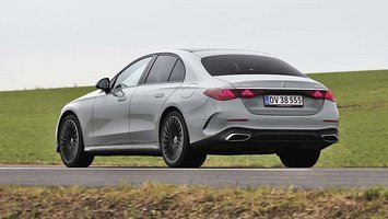 En sølvgrå Mercedes E-klasse set bagfra, mens den kører på en vej med græs i baggrunden