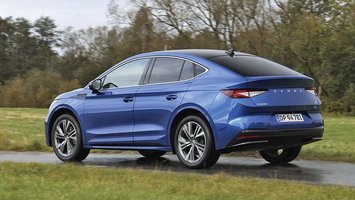 En blå Skoda Enyaq Coupé set bagfra, mens den kører på en landevej med græs i forgrunden