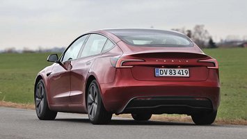 En rød Tesla Model 3 set bagfra, mens den holder foran en græsplæne.