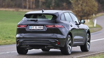 En sort Jaguar F-Pace set bagfra, mens den kører ind i et sving på en landevej med græs og træer i baggrunden