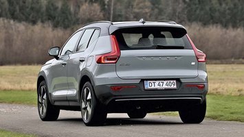 En grå Volvo XC40 elbil set bagfra, mens den kører på en landevej med træer i baggrunden