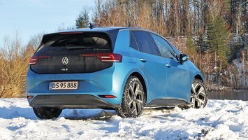 En blå VW ID.3 set bagfra holder i sne med en skovsø i baggrunden