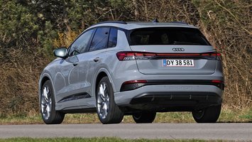 En grå Audi Q4 e-tron set bagfra kører på en vej med træer i baggrunden