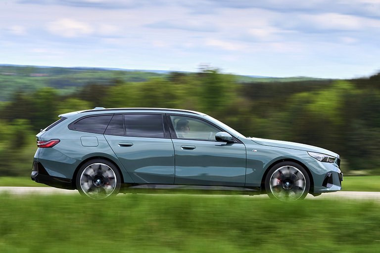 BMW i5 Touring set fra siden, mens den kører gennem et grønt landskab