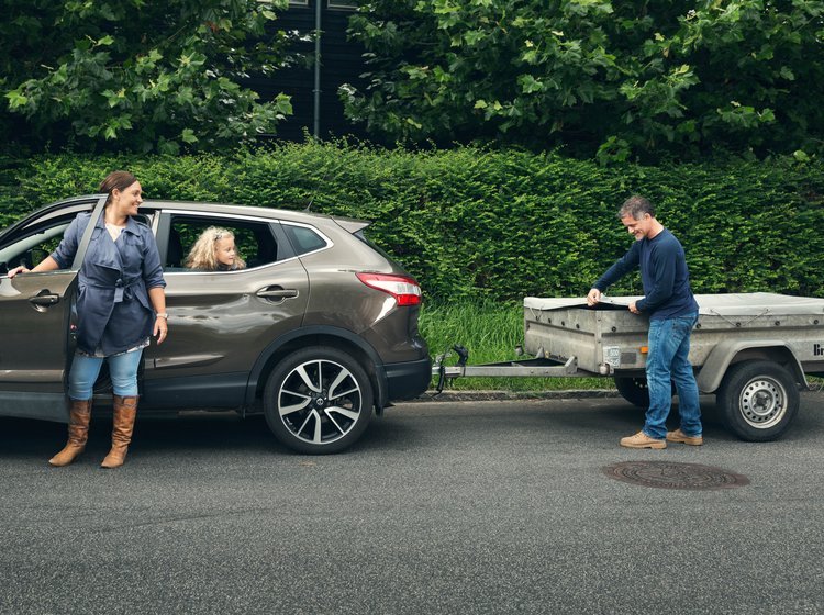Mand er ved at pakke trailer, mens kvinde er klar til at køre bilen. 