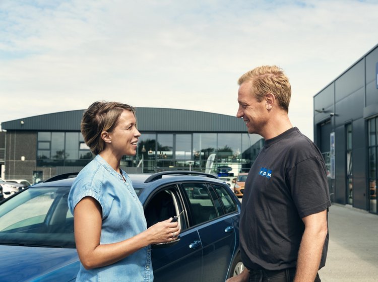 Bilist står sammen med mekaniker foran en bil udenfor.