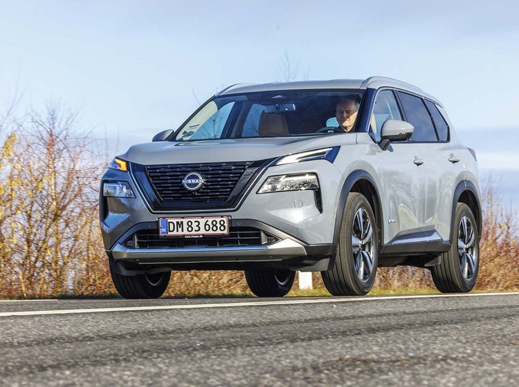 Nissan X-Trail kører på en vej med buskads i baggrunden