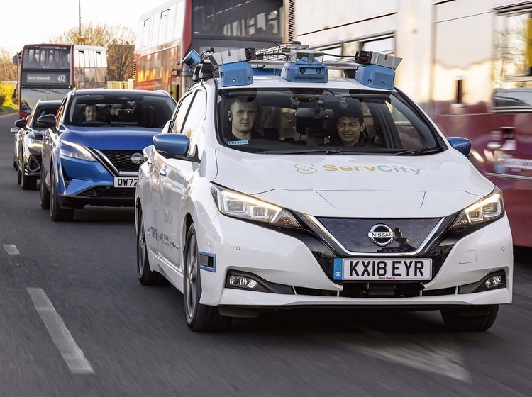 Selvkørende Nissan Leaf kører på vejen i Lodon omgivet af røde London-busser