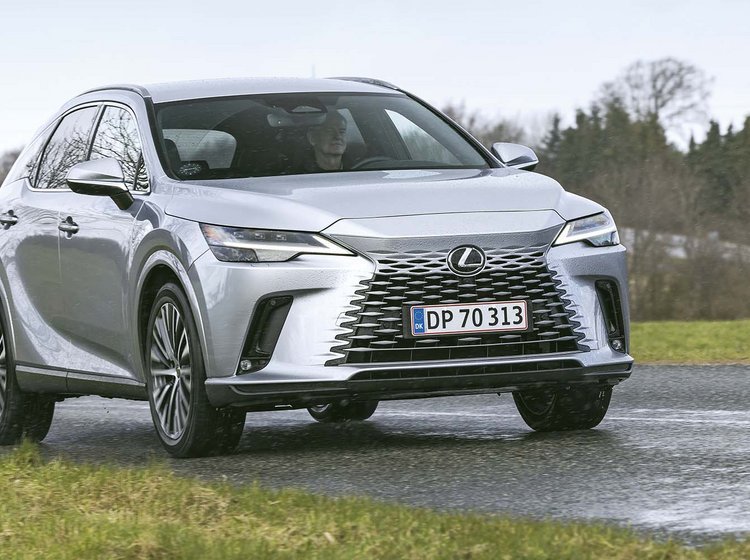 Sølvgrå Lexus RX plugin-hybrid kører på landevej med græs i forgrunden