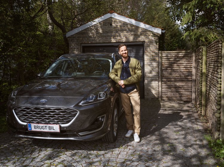 Mand står ved siden af sin brugte bil, som holder i en carport