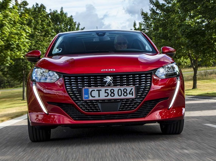 Rød Peugeot 208 kører på landevej med træer i baggrunden. 