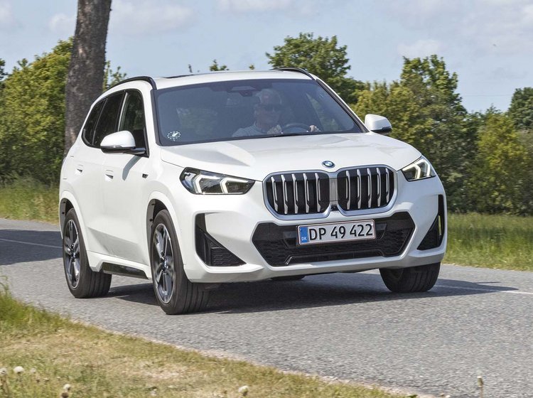 En hvis BMW X1 kører på en landevej med træer i baggrunden