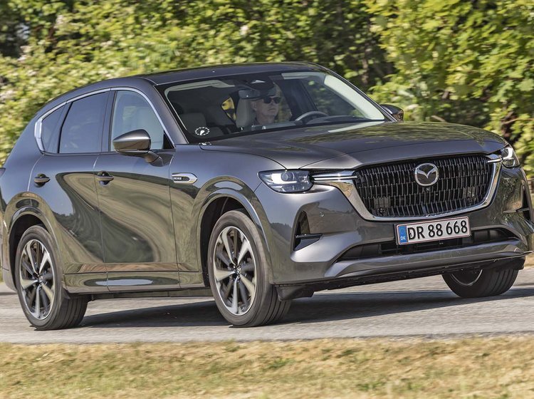 En Mazda CX-60 med stor dieselmotor kører på en landevej med træer i baggrunden