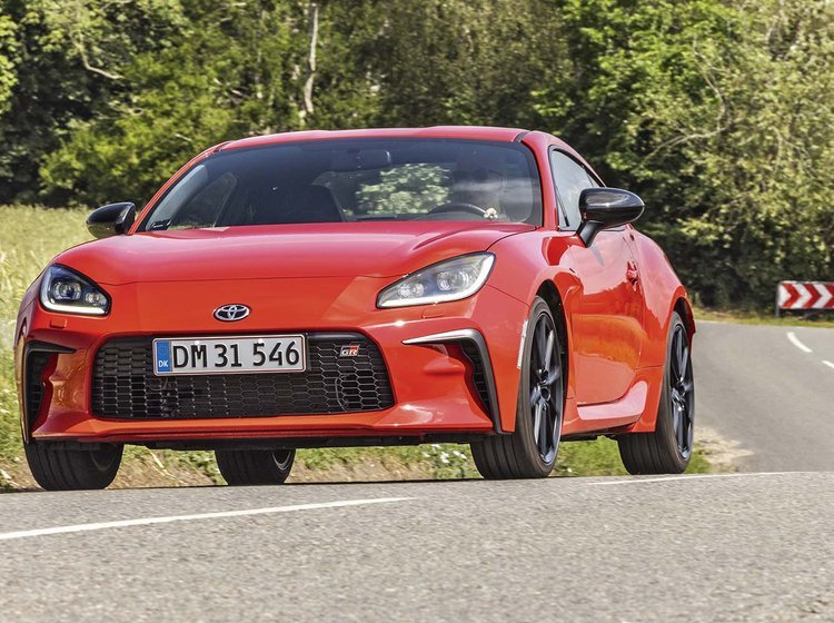 Rød Toyota GR86 kører på landevej med træer i baggrunden. 