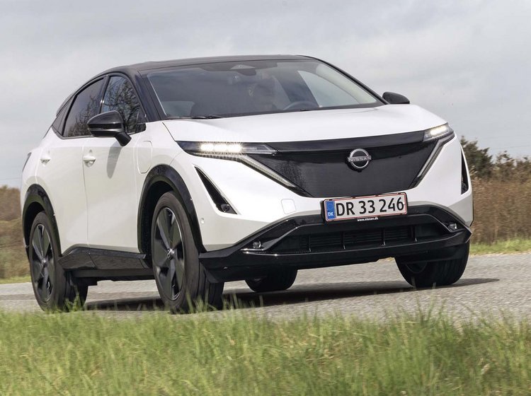 En hvid Nissan Ariya elbil kører på en landevej.
