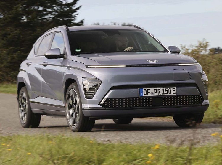 Elbilen Hyundai Kona kører på en landevej med græs foran og bagved.