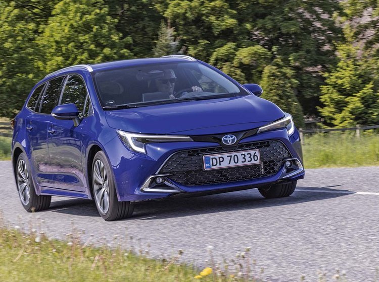 Hybridbilen Toyota Corolla Touring Sports kører på en landevej med træer i baggrunden