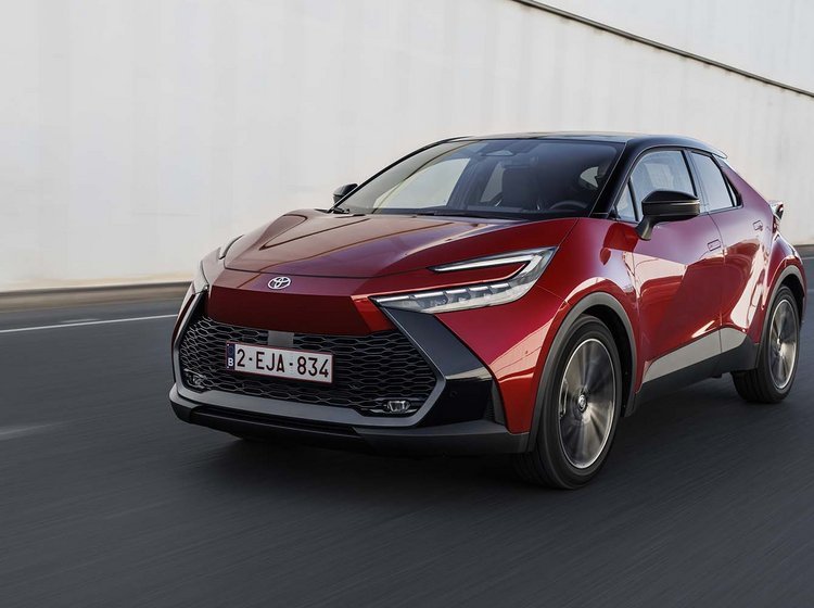 En rød Toyota C-HR kører på en motorvej med støjværn i baggrunden