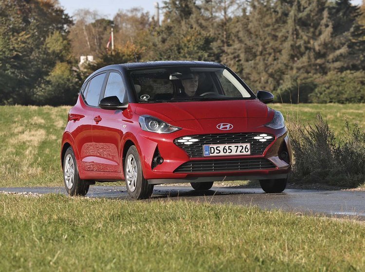 En rød Hyundai i10 kører på en landevej med træer i baggrunden