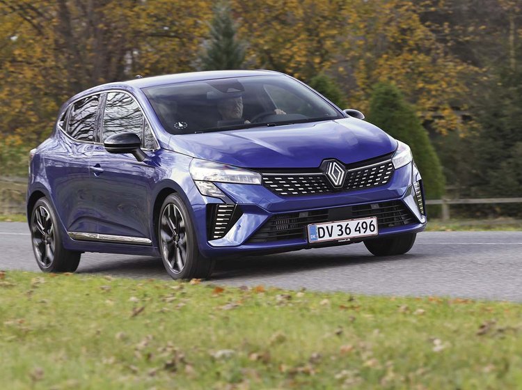 En blå Renault Clio kører på en landevej med græs i forgrunden og træer i baggrunden