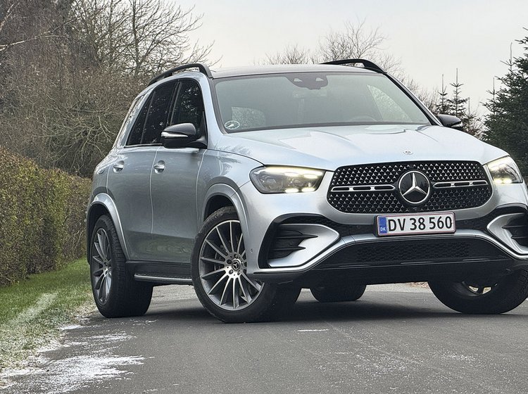 En sølvgrå Mercedes-Benz GLE holder på en vej med en hæk i baggrunden.