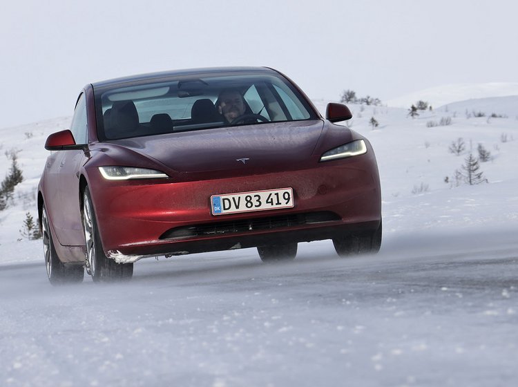 En rød Tesla Model 3 set forfra kører i snelandskab