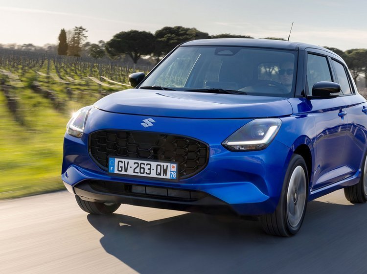Blå Suzuki Swift kører på en vej med vinmarker i baggrunden