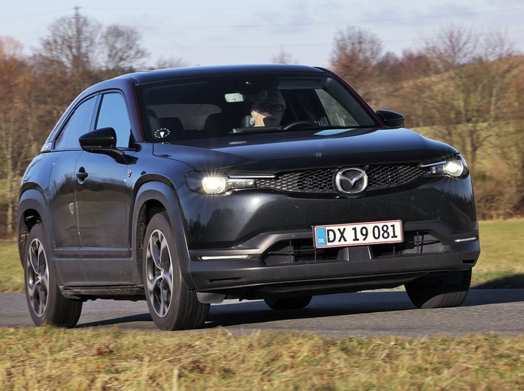 En sort Mazda MX-30 R-EV kører på en landevej med træer og græs i baggruden