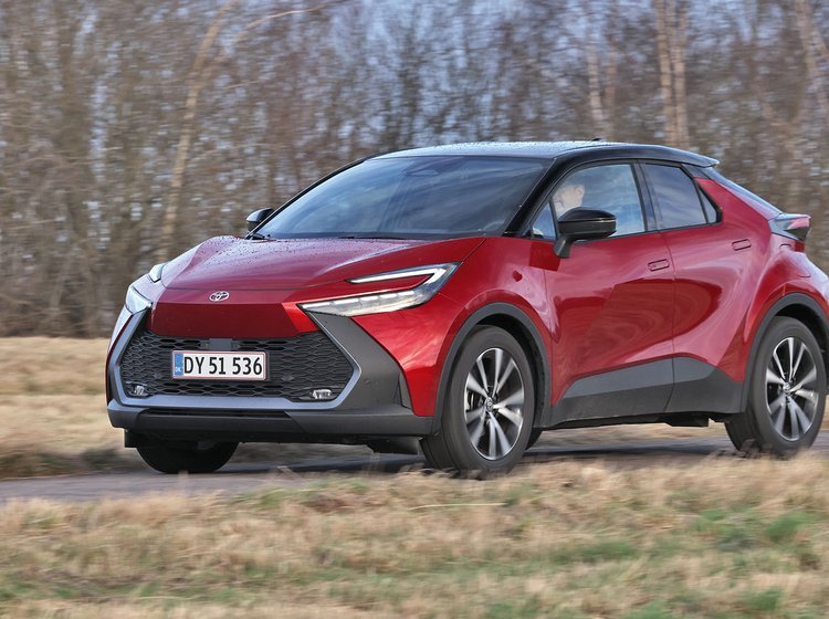 En rød Toyota C-HR kører på landevej med træer i baggrunden