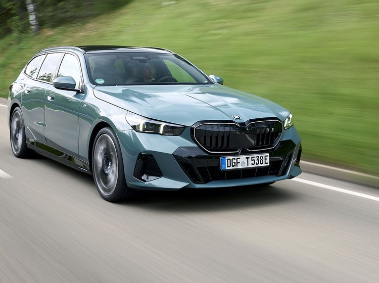 Grøn BMW i5 Touring kører på en vej med græs i baggrunden
