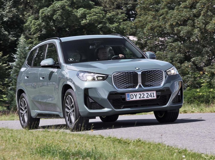 BMW iX1 kører på en vej med træer i baggrunden