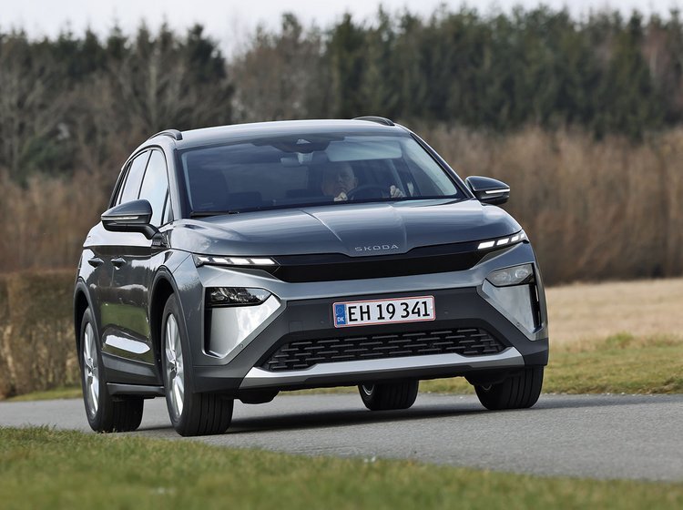 Skoda Elroq 50 set forfra, mens den kører på en landevej med træer og marker i baggrunden