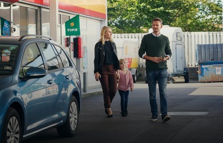 Familie går hen til bil på tankstation. 
