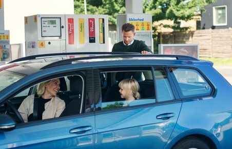 Bil med familie holder på tankstation og får påfyldt brændstof. 