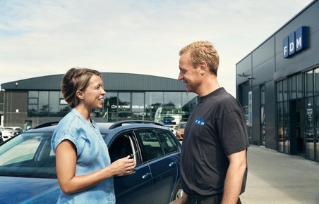 Bilist står sammen med mekaniker foran en bil udenfor.
