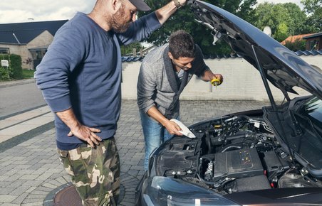 To mænd kigger ned i motorrummet på en bil. 