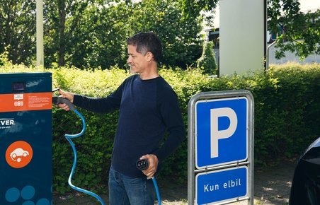  Mand står ved en oplader til elbiler og har forbundet et kabel til opladeren. 