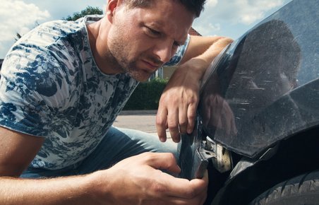 Mand kigger på sin bil, der har fået en skade efter en ulykke. 