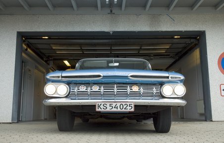 Ældre bil parkeret foran garage. 