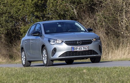 En sølvgrå Opel Corsa kører på landevej med træer i baggrunden