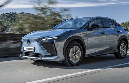 En Lexus RZ kører på bjergvej med udsigt til havet i baggrunden